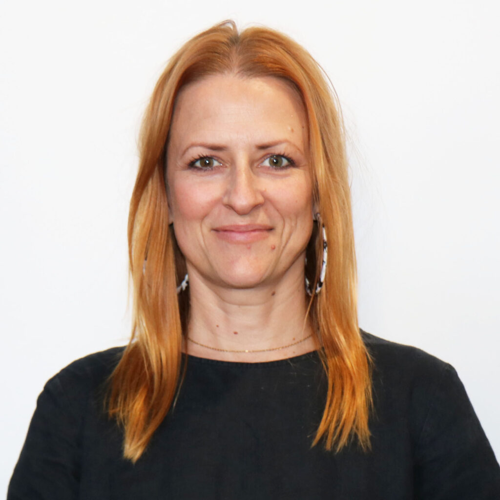 Carla Steele, Long orange hair, and wearing a black top with big hoop earrings.
