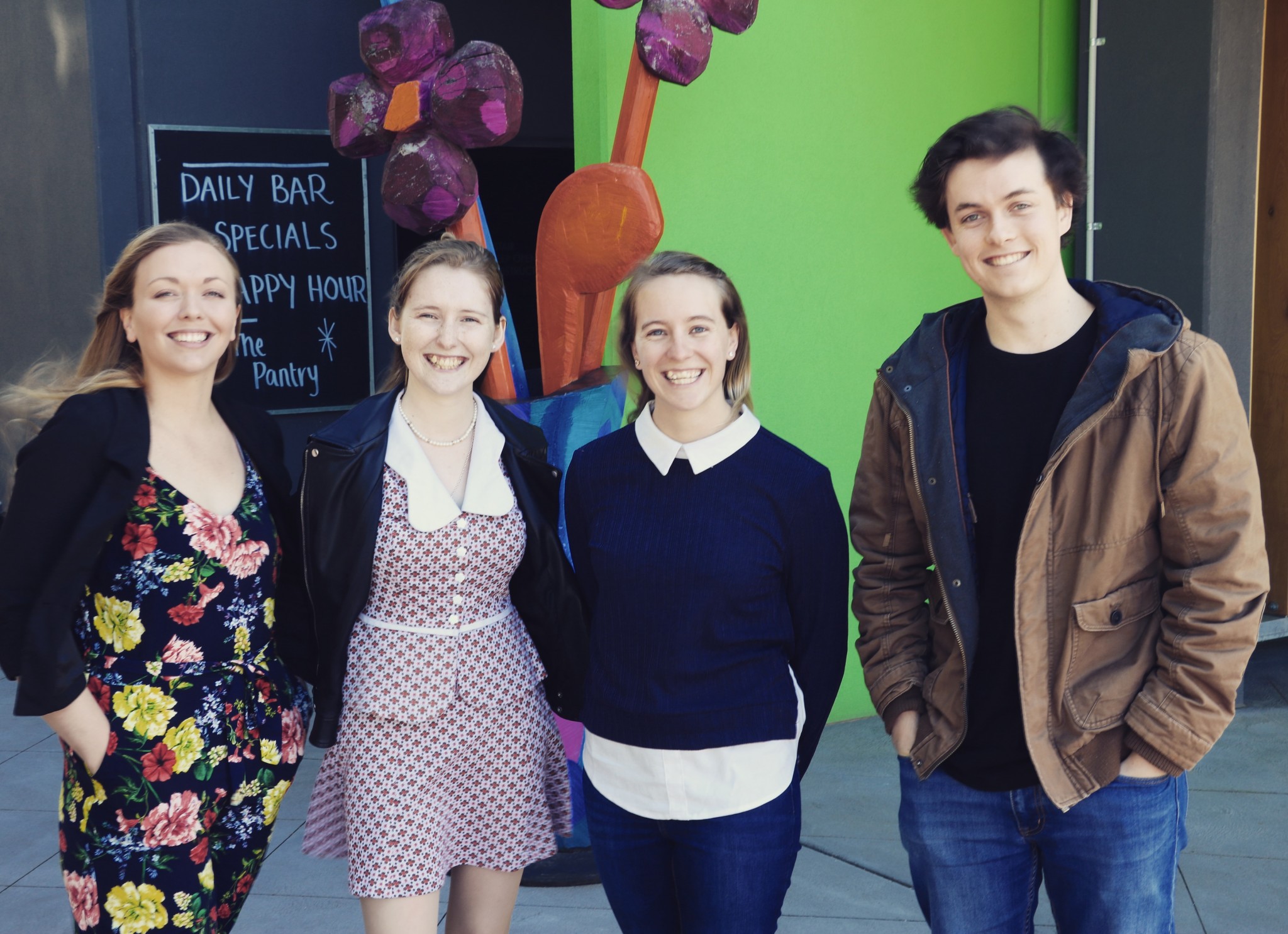 Four people dressed casually stand outside a building and stand together for a photo.