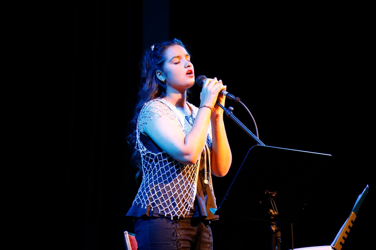Person on stage sings into microphone, eyes closed.