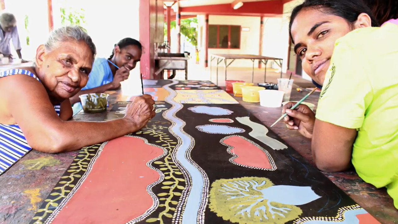 Three people work together on an aboriginal dot work painting.
