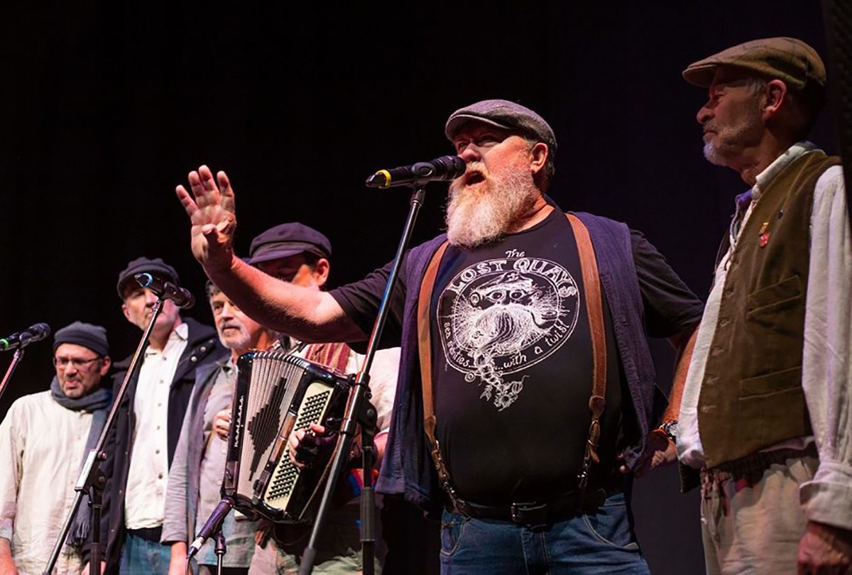 Group of people on stage with one person speaking into a microphone.