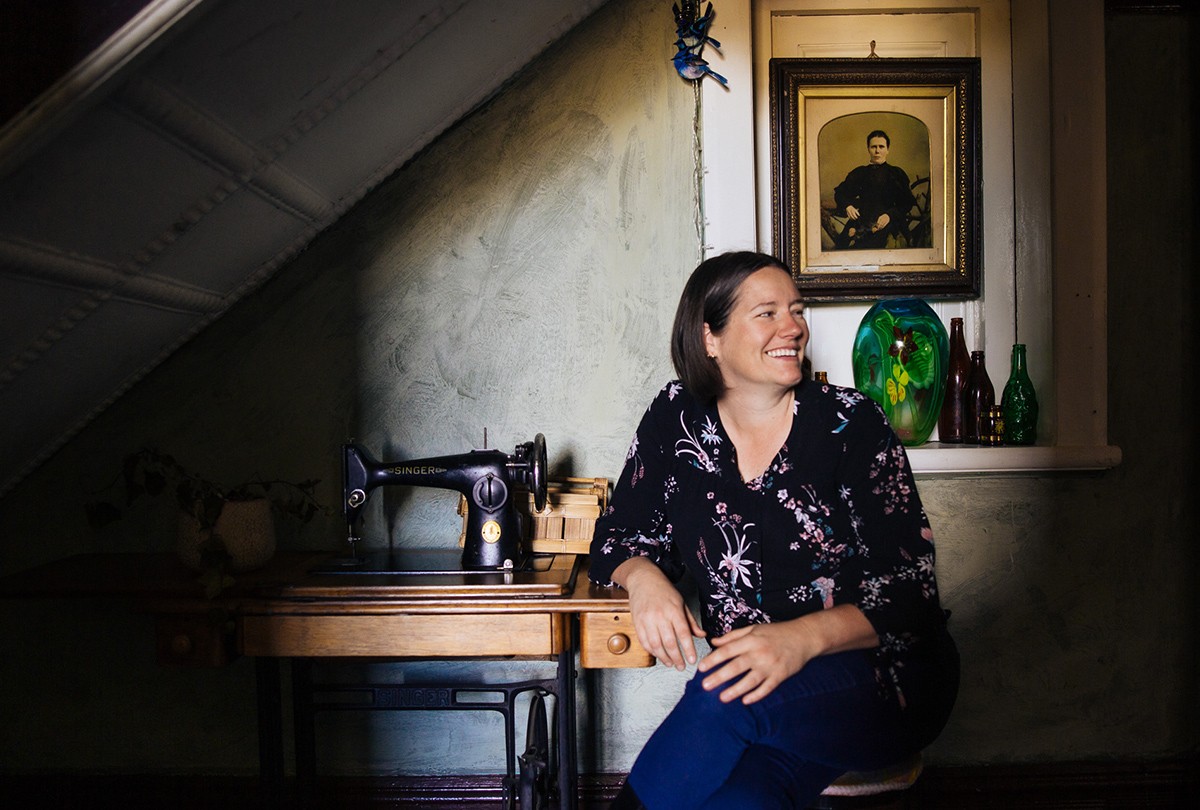 Person with short dark hair sits next to an old Singer sewing machine.
