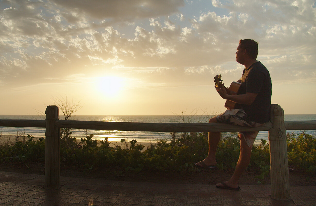 Person plays guitar at sunset by the beach.