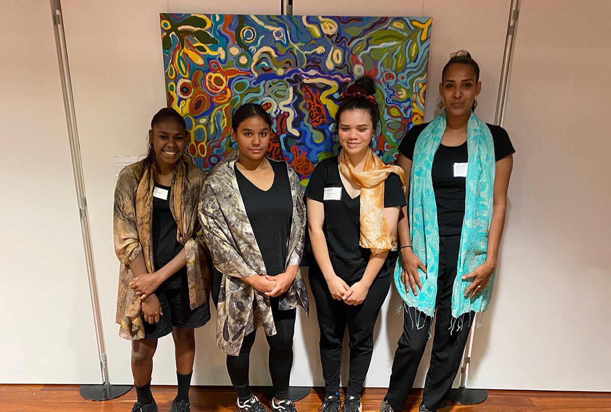 Four people stand in front of an abstract nature artwork.