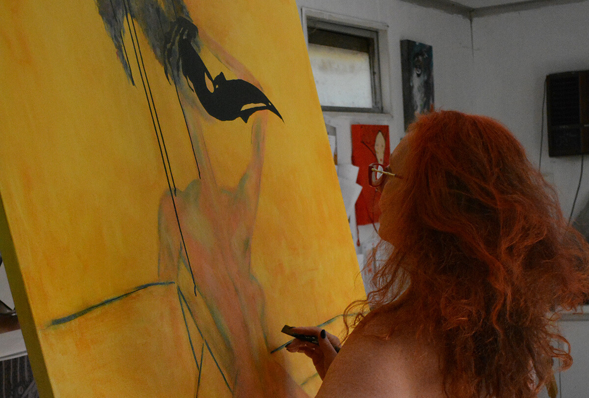 Person with red hair works on a painting in a studio.