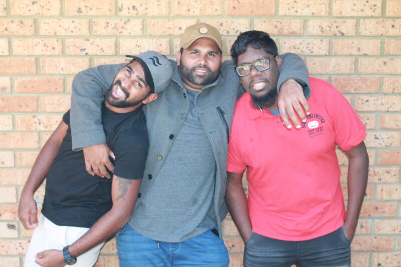 Three people, middle person has their arms around both people on their side.