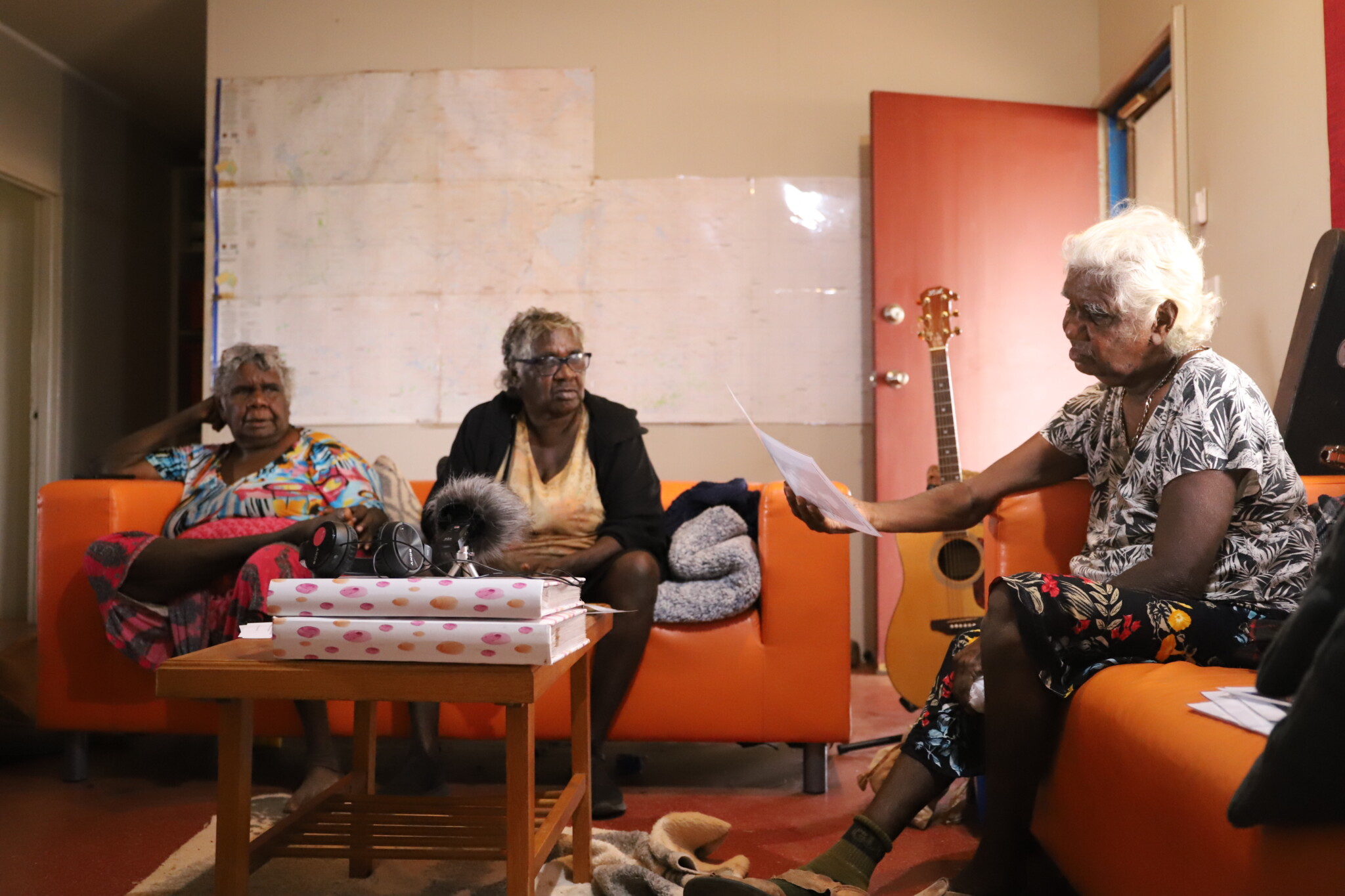 Three indigenous women sit on couches, sharing stories and photos with each other