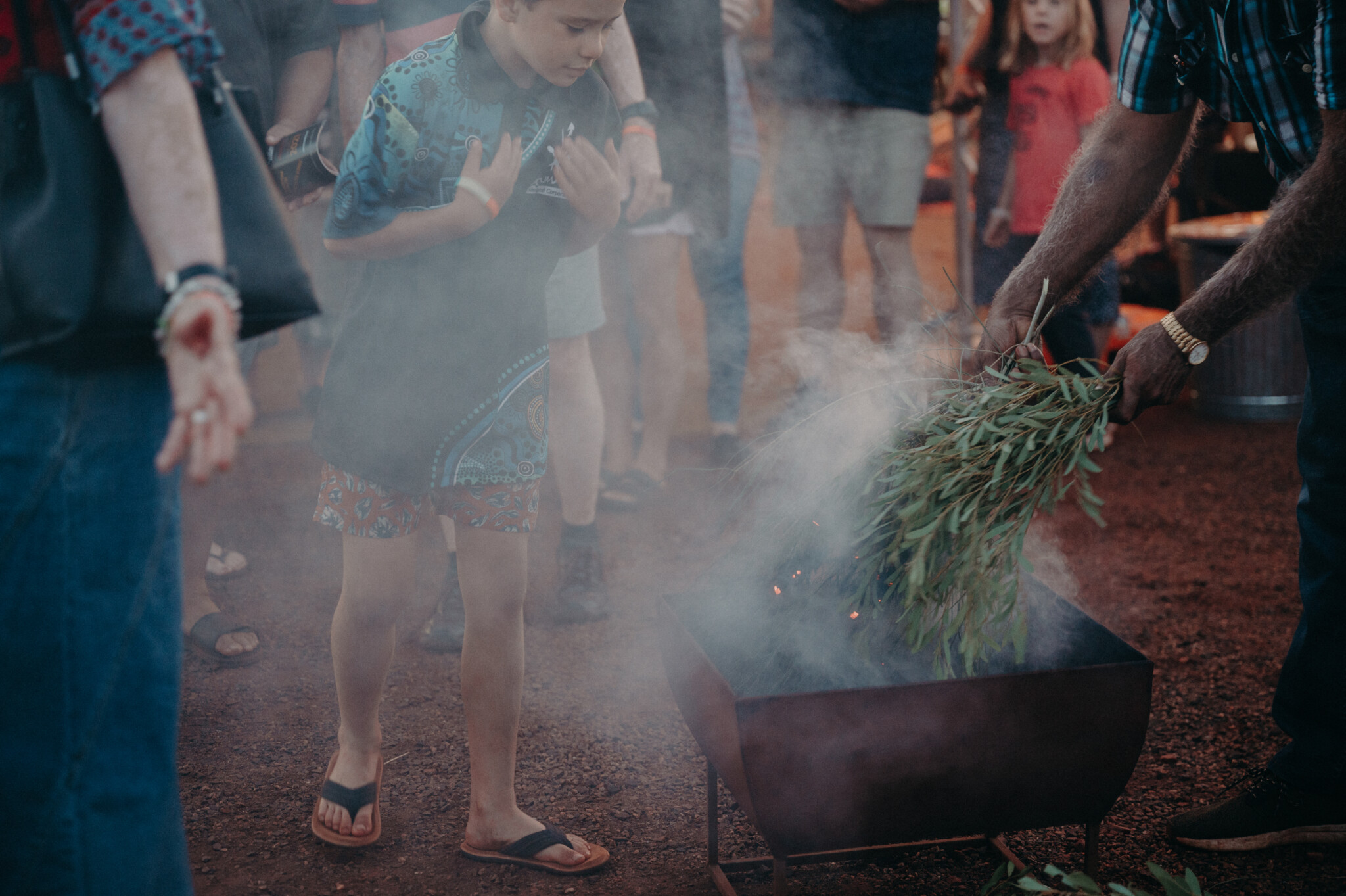 A young boy approaches the smoking ceremony, the area is filled with smoke from smouldering native plants