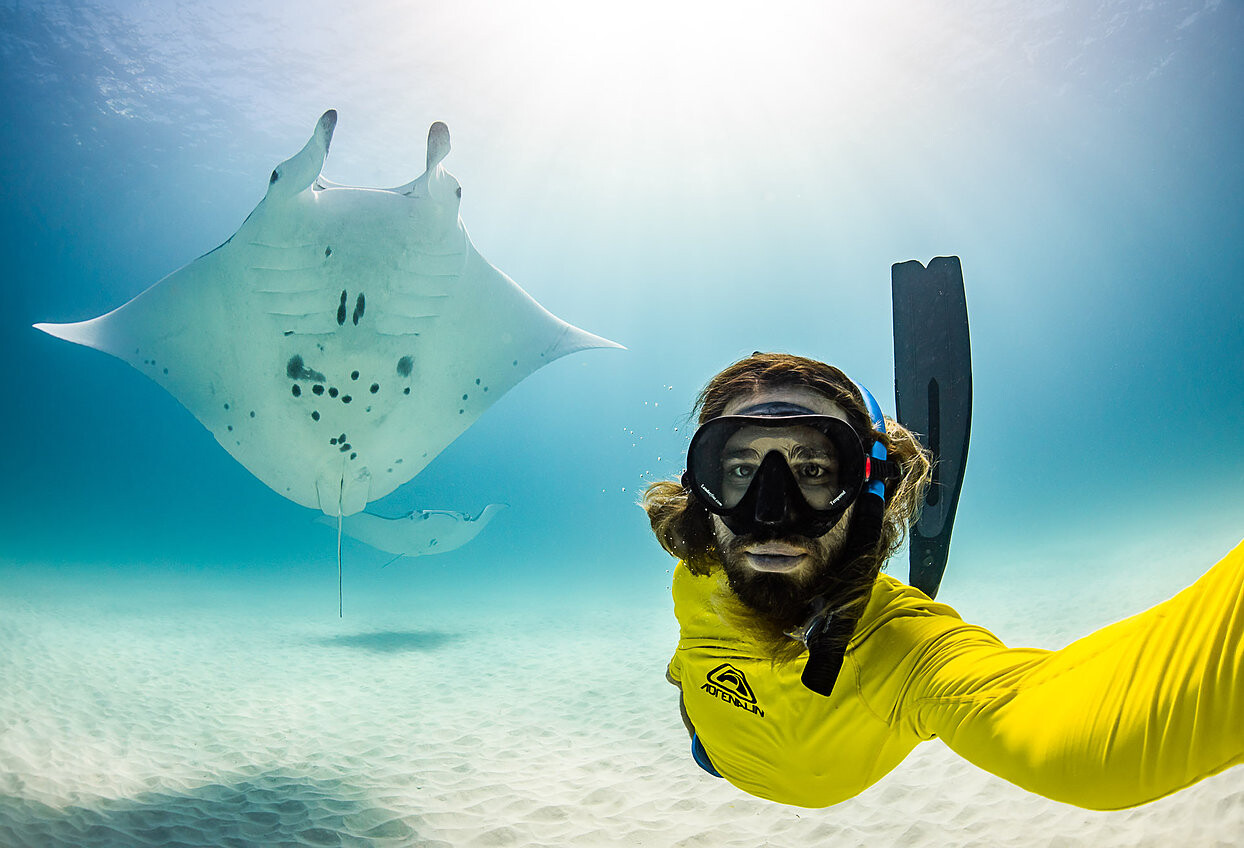 Selfie style photo of a person on the right wearing bright yellow and a stingray on the left.