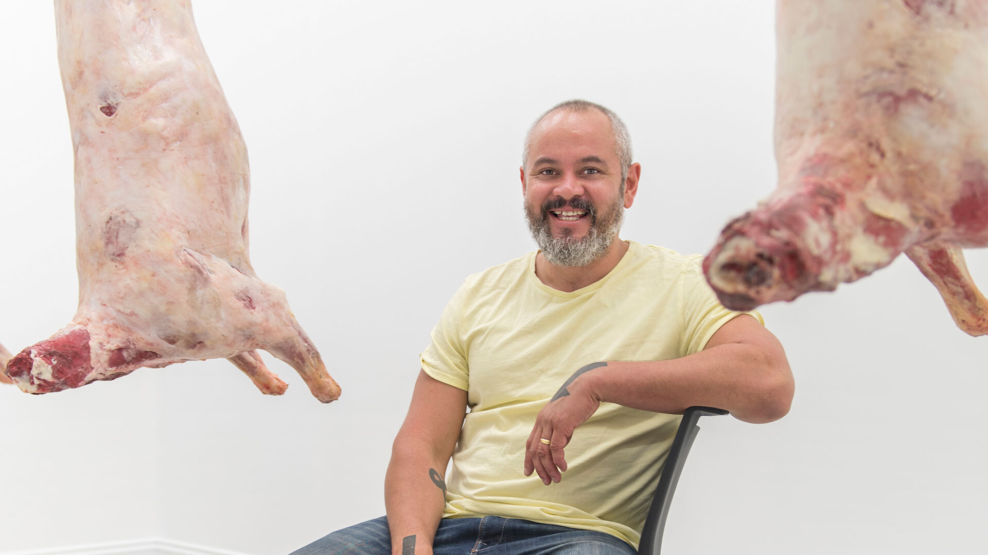 Abdul-Rahman Abdullah sits in gallery space with his artwork