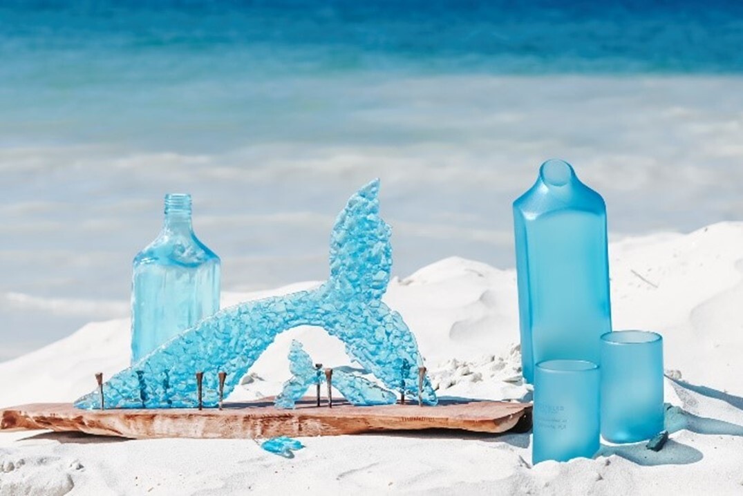 Bright blue carafe, glasswear, bottle, and whale scultpure on the sands of the beach