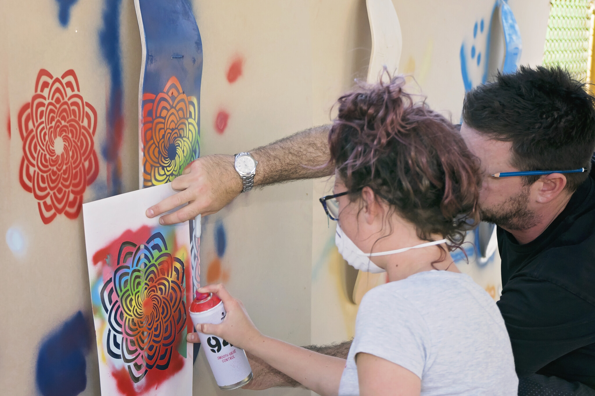 Adult and teenager work together to spray paint patterns onto a wall.