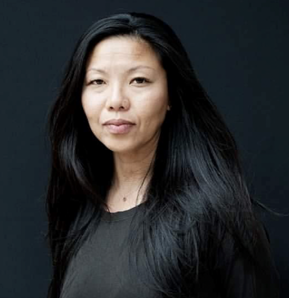 Woman with long dark hair standing against a grey background.