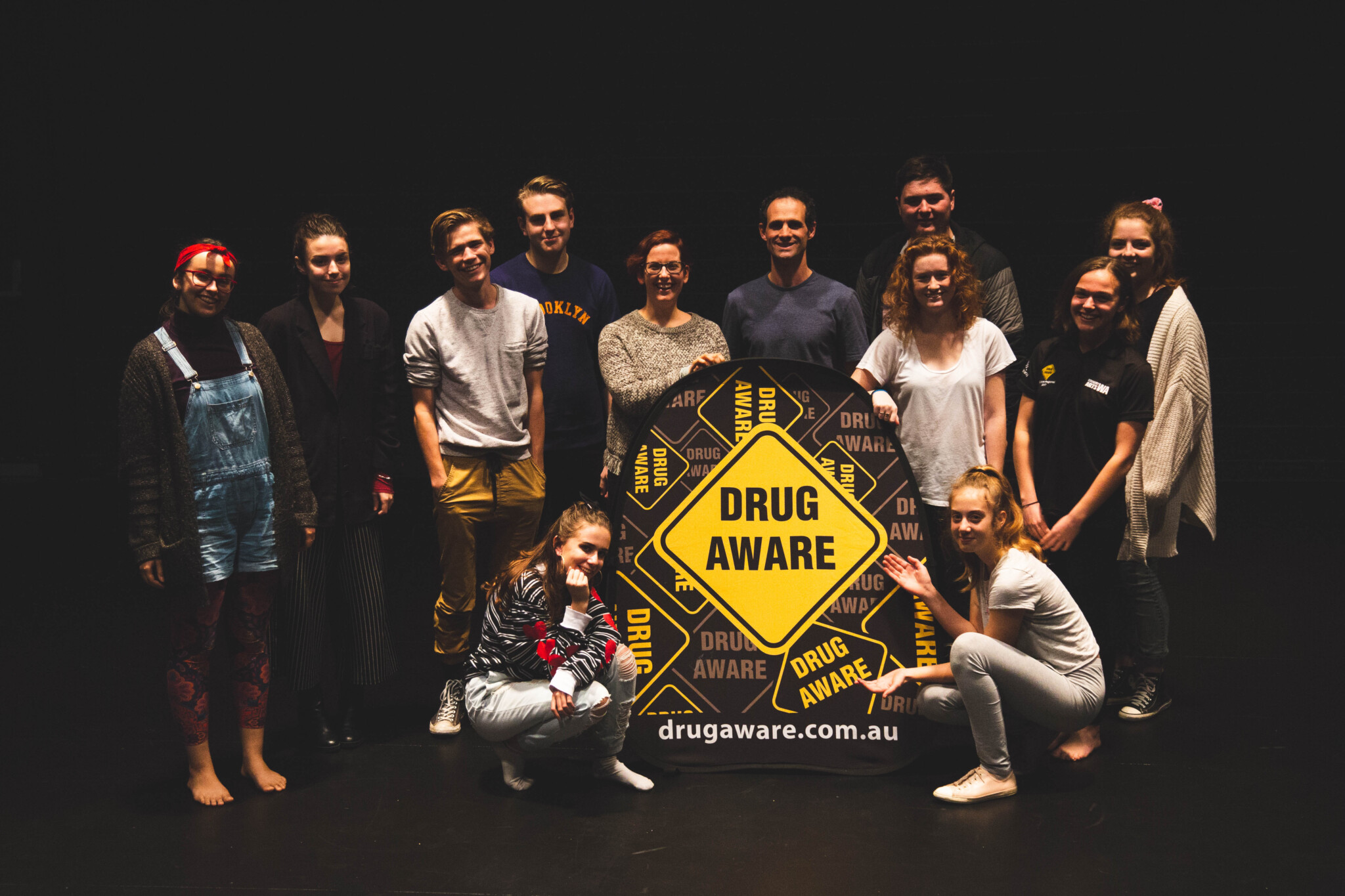 Indoor group photo of teenagers stnding around the Drug Aware banner.