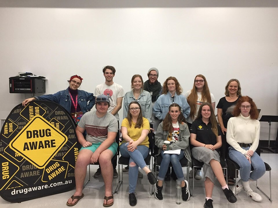 teengers seated for a group photo indoors, next to drug aware banner.