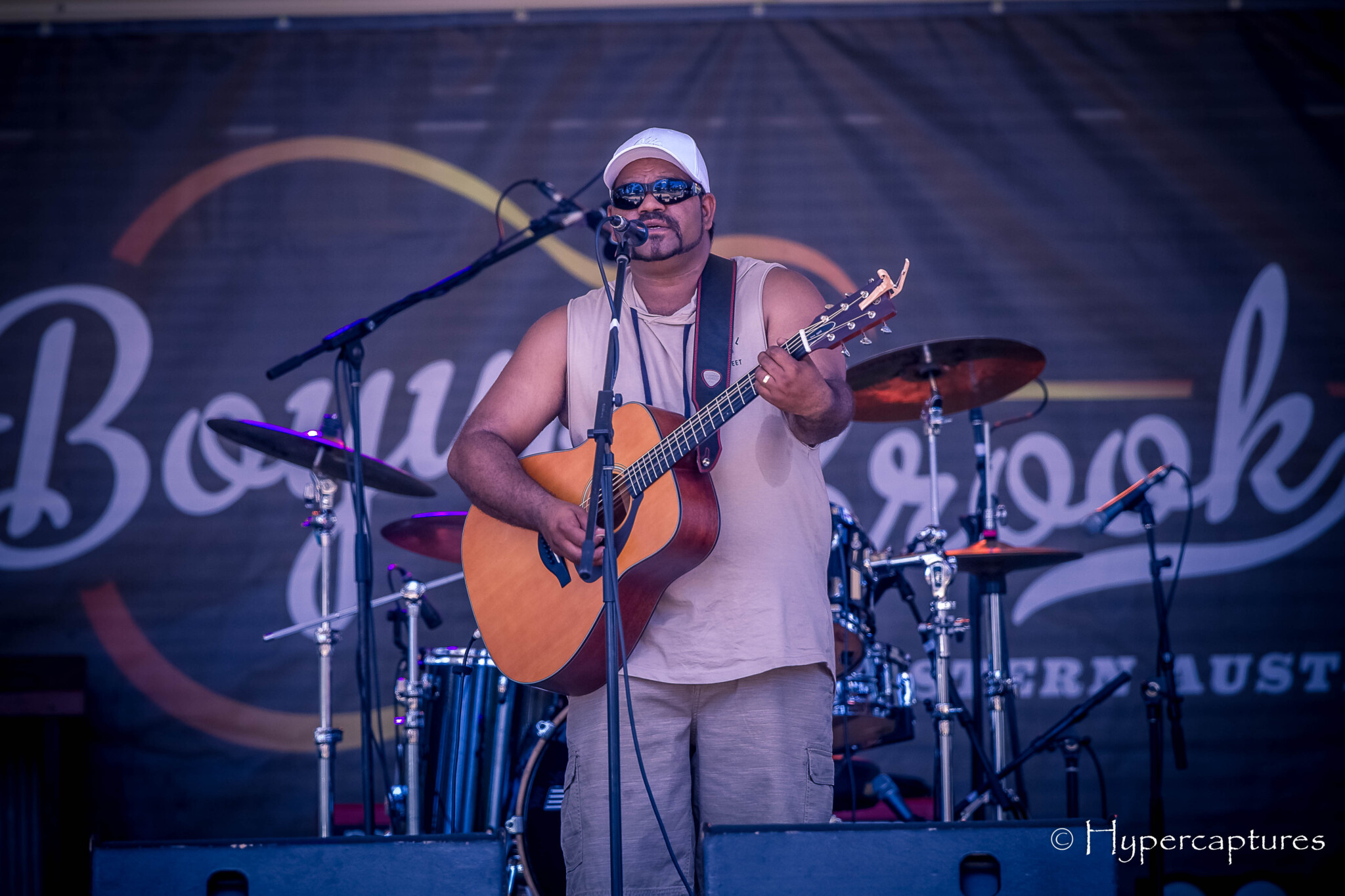 First nations man stands on stage with microphone and guitar.