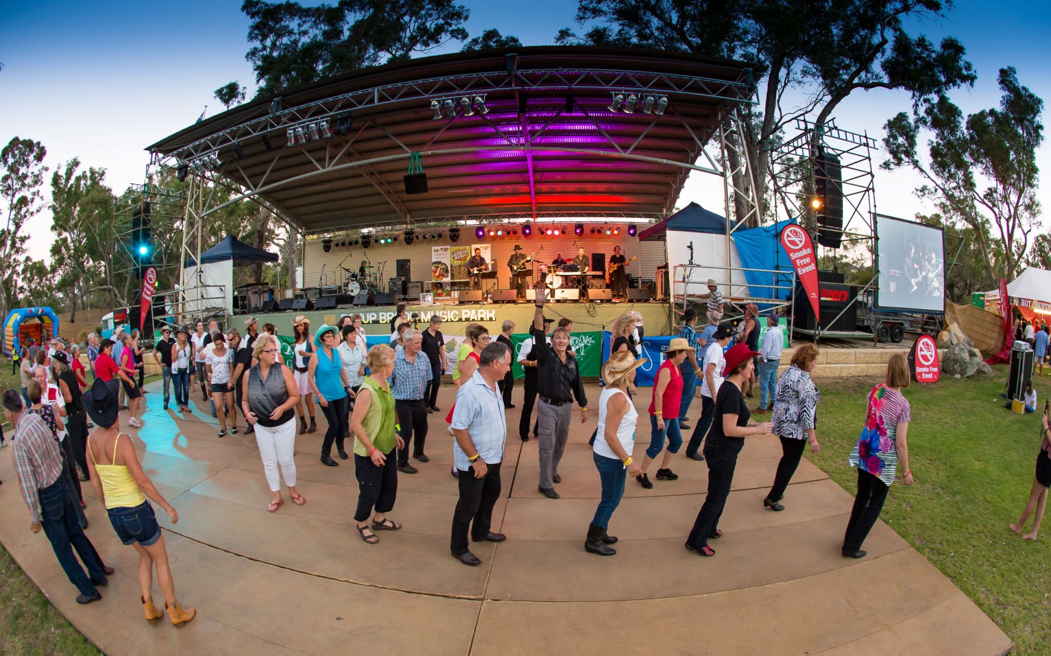 Fish-eye photo of a crowd of people bootscooting as a band plays in the marquee in front