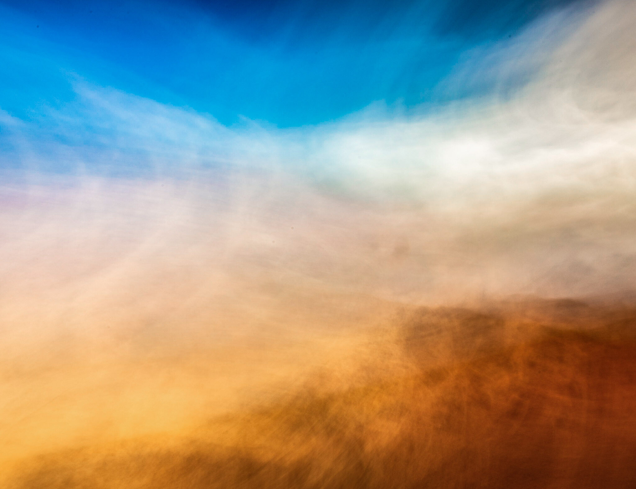 Abstract landscape of the sky and clouds as they blend from bright blue to dark orange.