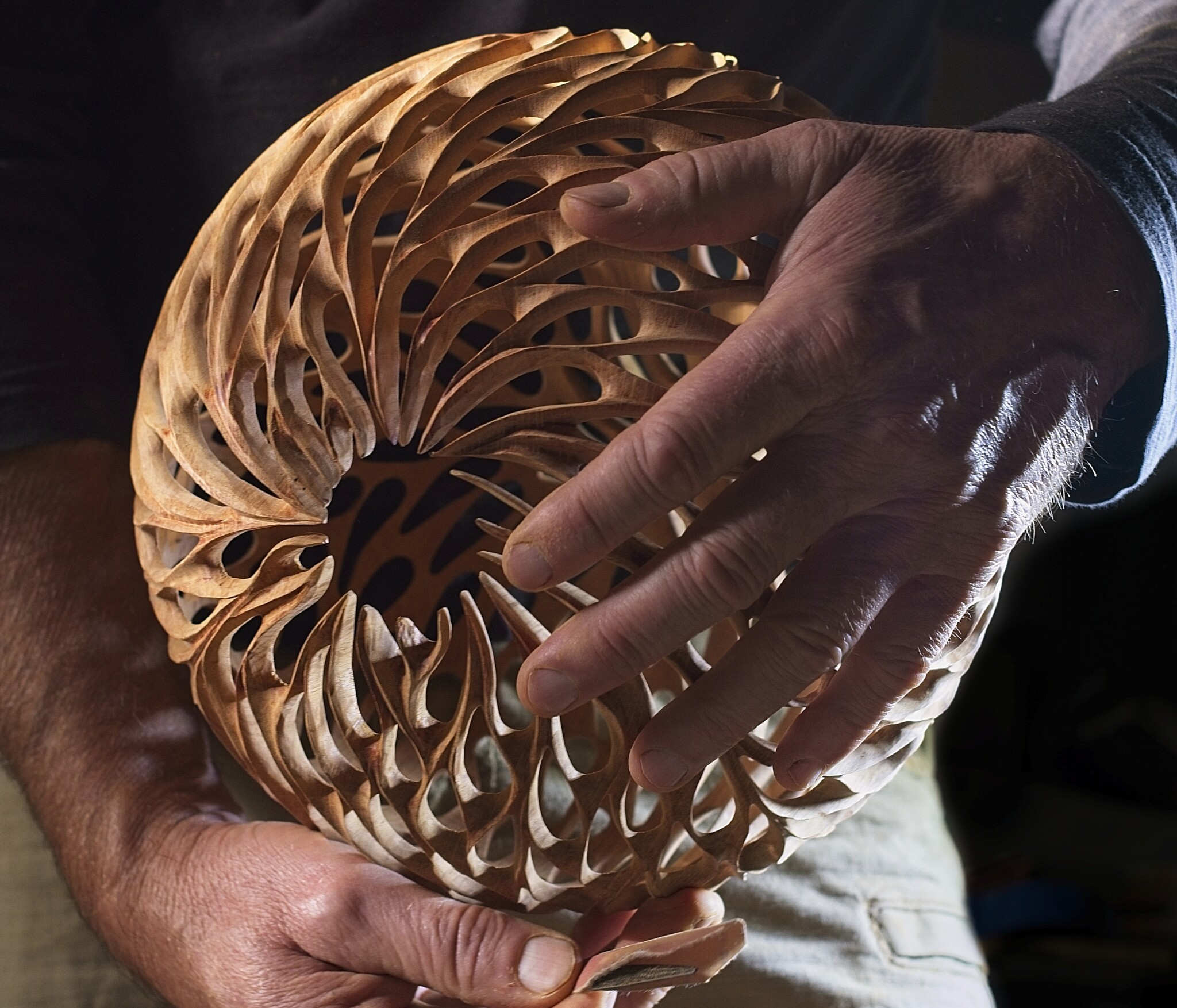 Close-up of Neil's hands holding a wooden spherical sculpture. The sculpture is hollow and made with many perforated pieces.