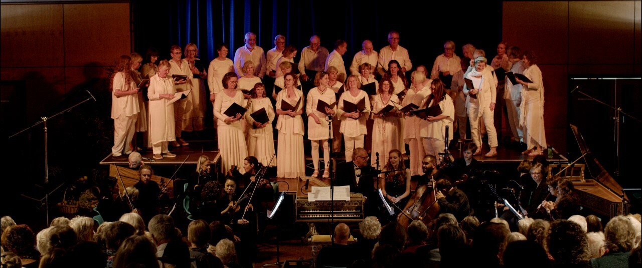 Choir and Orchestra gathered on a small stage in front of a seated audience.