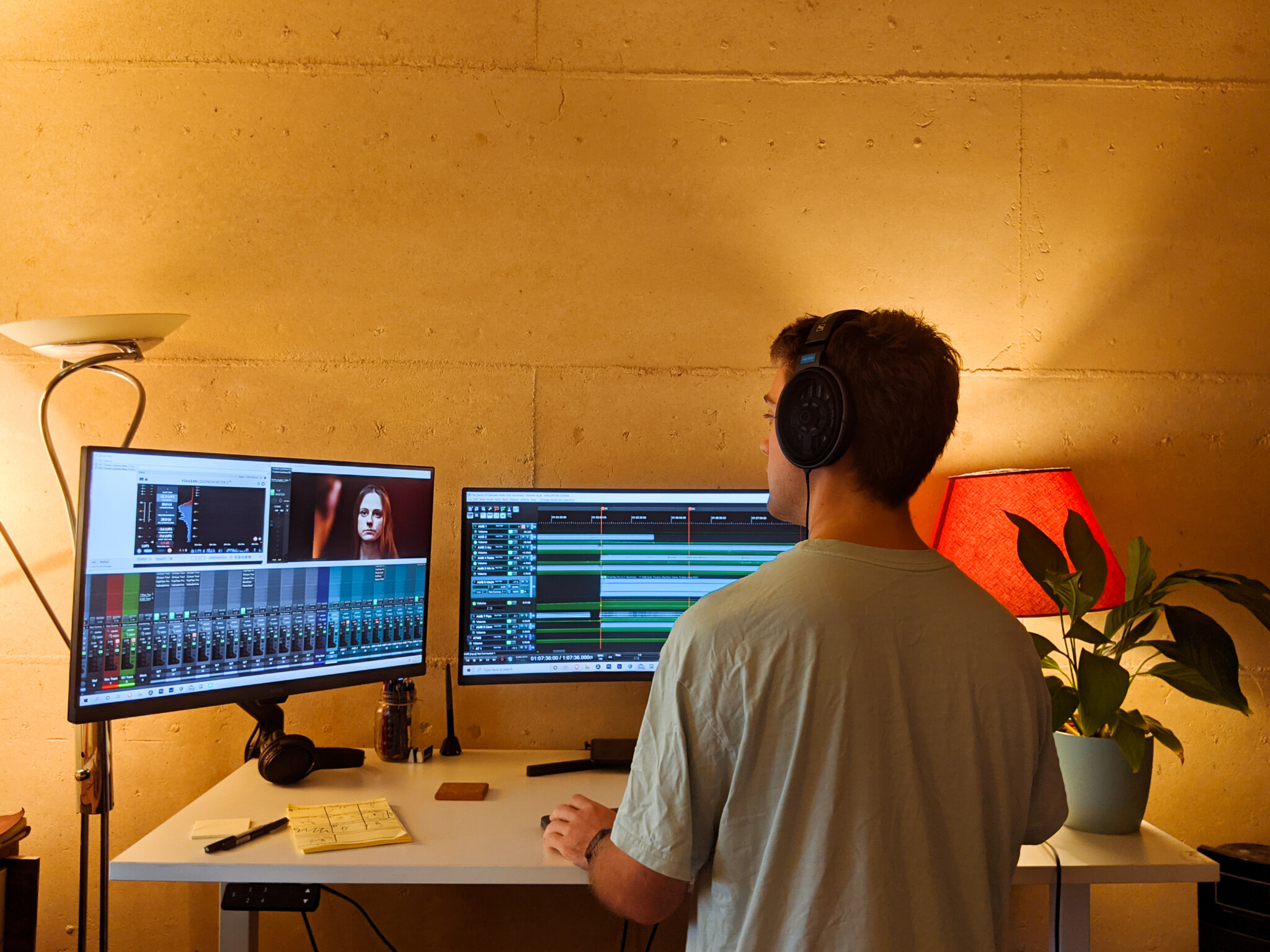 A young man stands at a desk, editing film on two computer monitors.