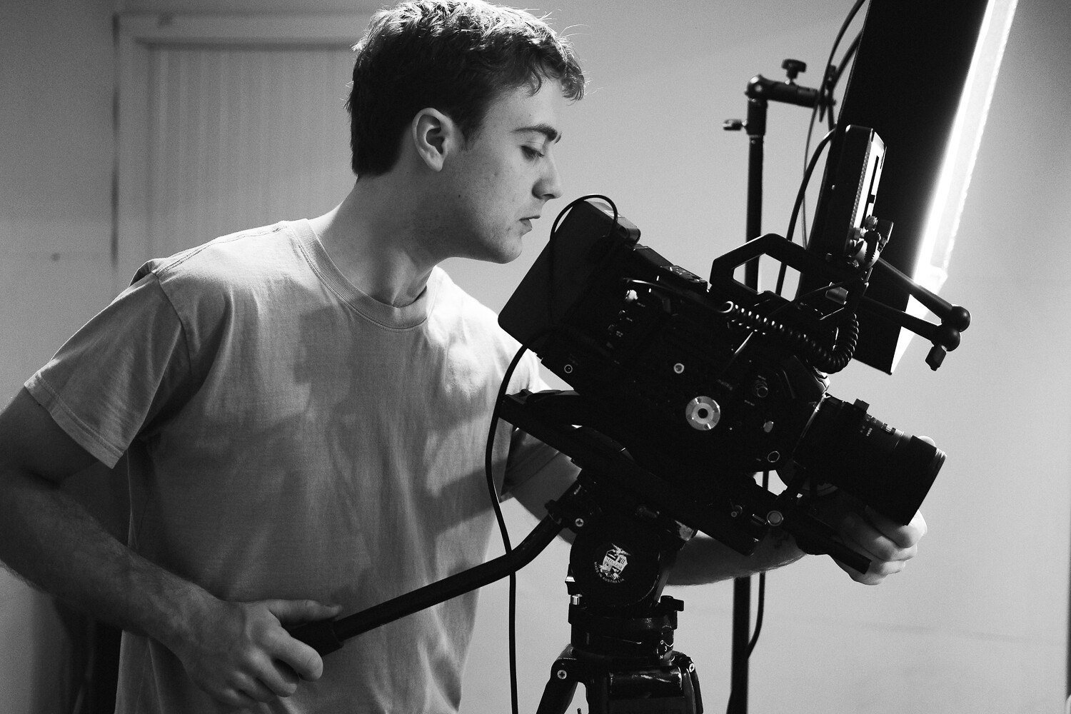 Black and white photo of a young man filming using a large camera.