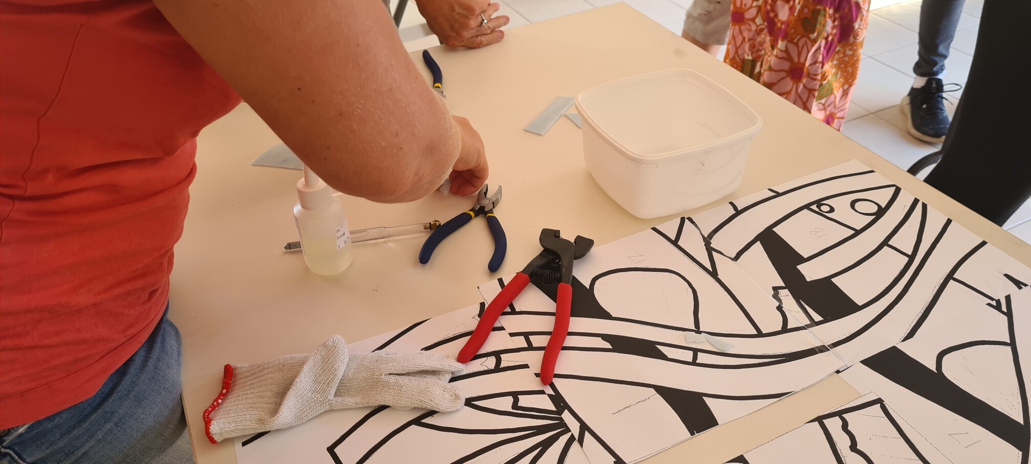 Paper templates for glass mosaic work, tools lay on top and there are hands making a demonstration.