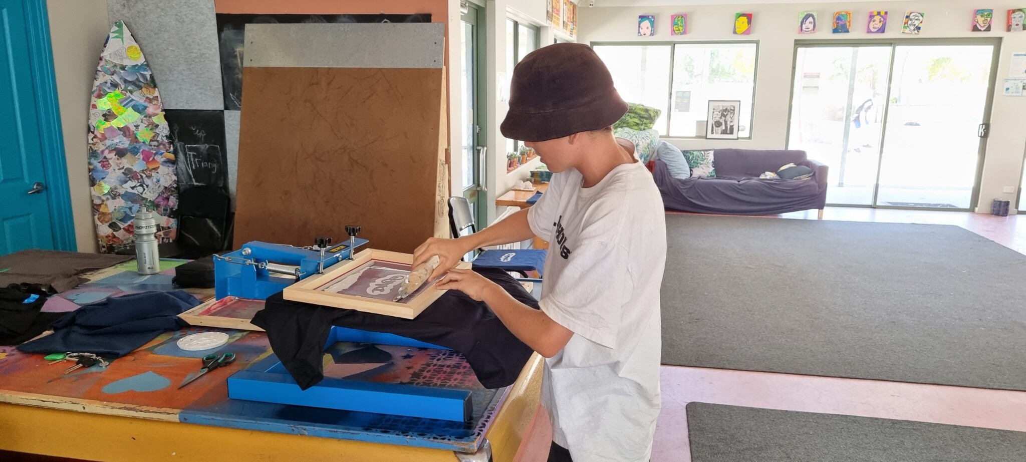 A young boy wearing a bucket hat screenprinting a T-Shirt