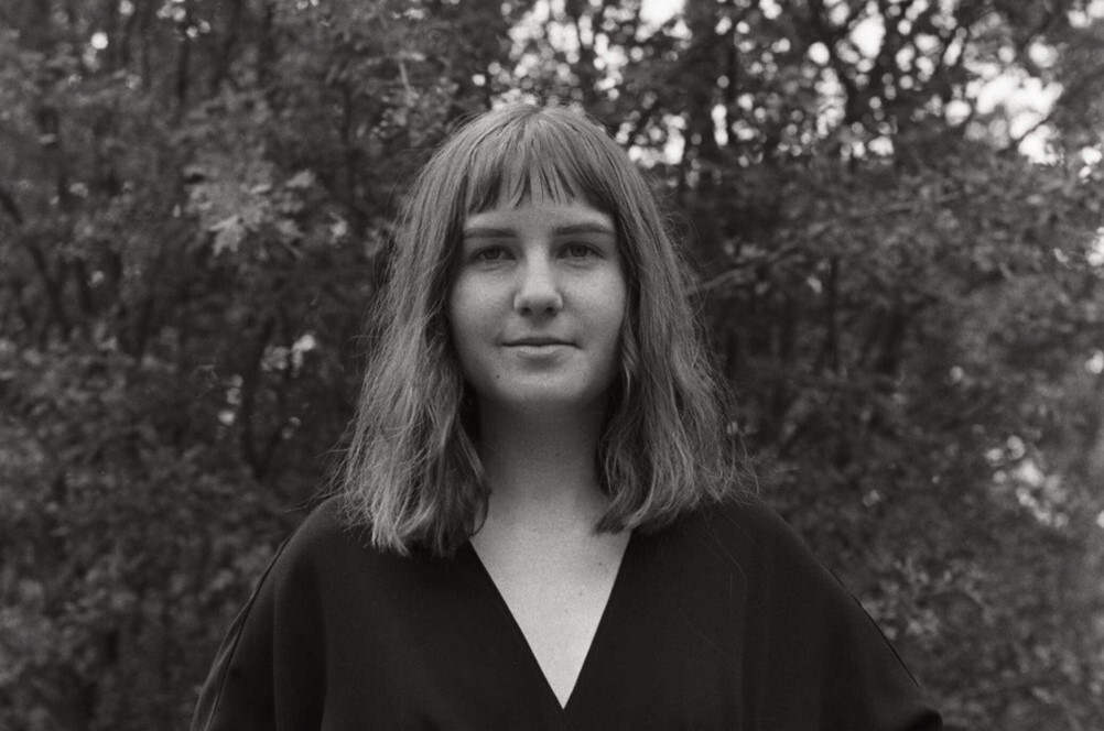 Black and white headshot of Rose Barton. She has shoulder length hair, short bangs and wears a black shirt.