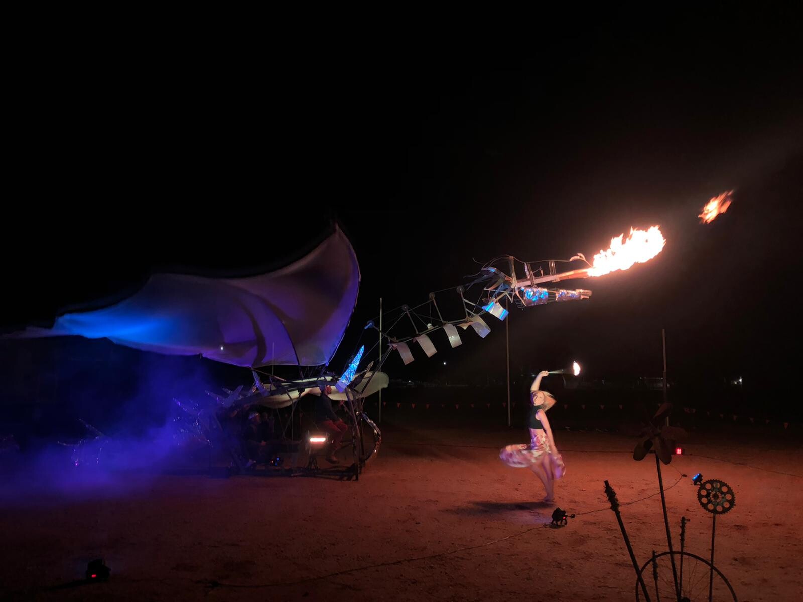 Mechanical dragon breathing fire while Miranda dances under it holing a fire baton.