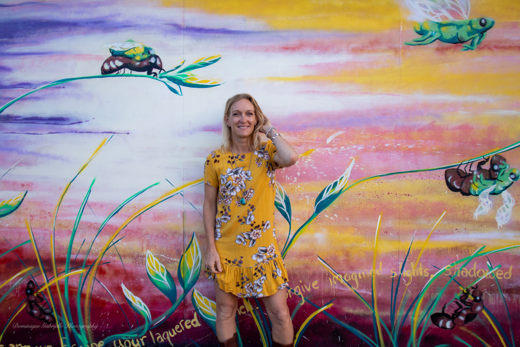 Woman in yellow floral dress stands in front of a mural painted on a wall.