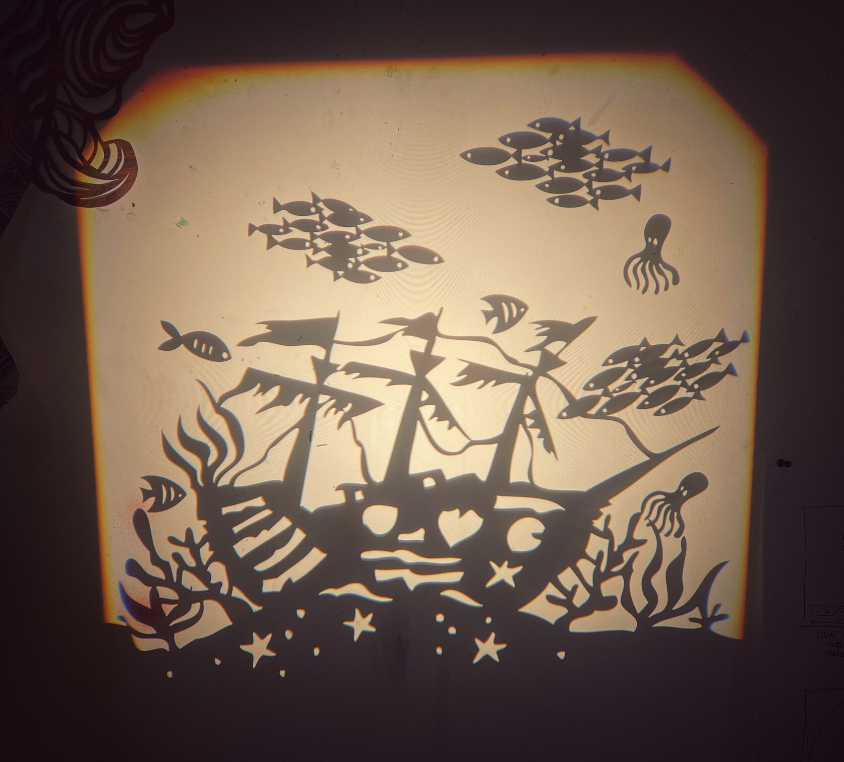 light projection of a sunken ship with sea creatures swimming around.