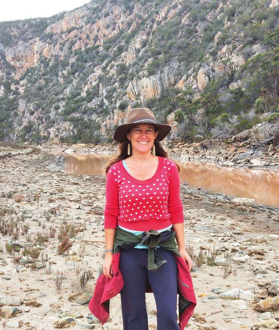 Renee wears a brown wide-brimmed hat, pink top with white polka dots, jeans, and has a green and pink jacket wrapped around her waist. 