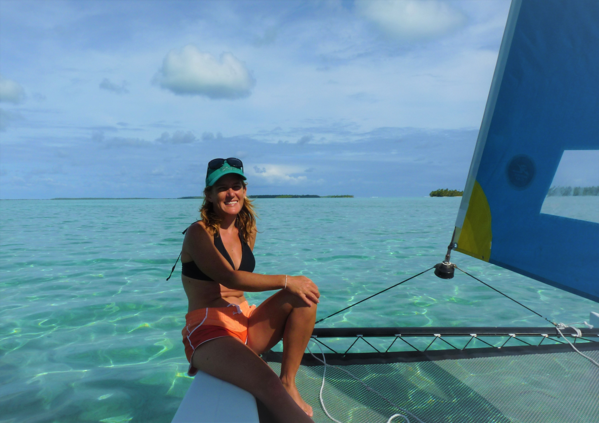 Renee wears bathers and sits on a boat with clear blue water behind her.