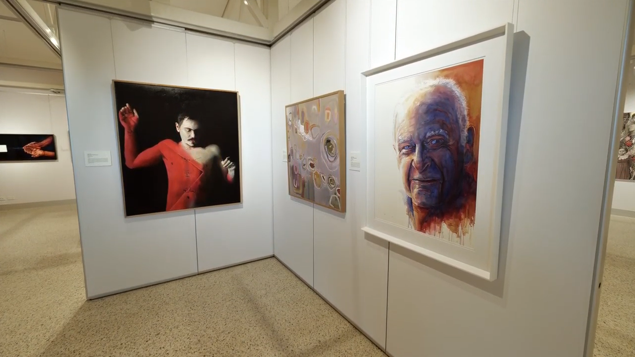 Art gallery with three paintings: a red figure with raised hand, abstract shapes in the center, and a vibrant, partially obscured portrait.
