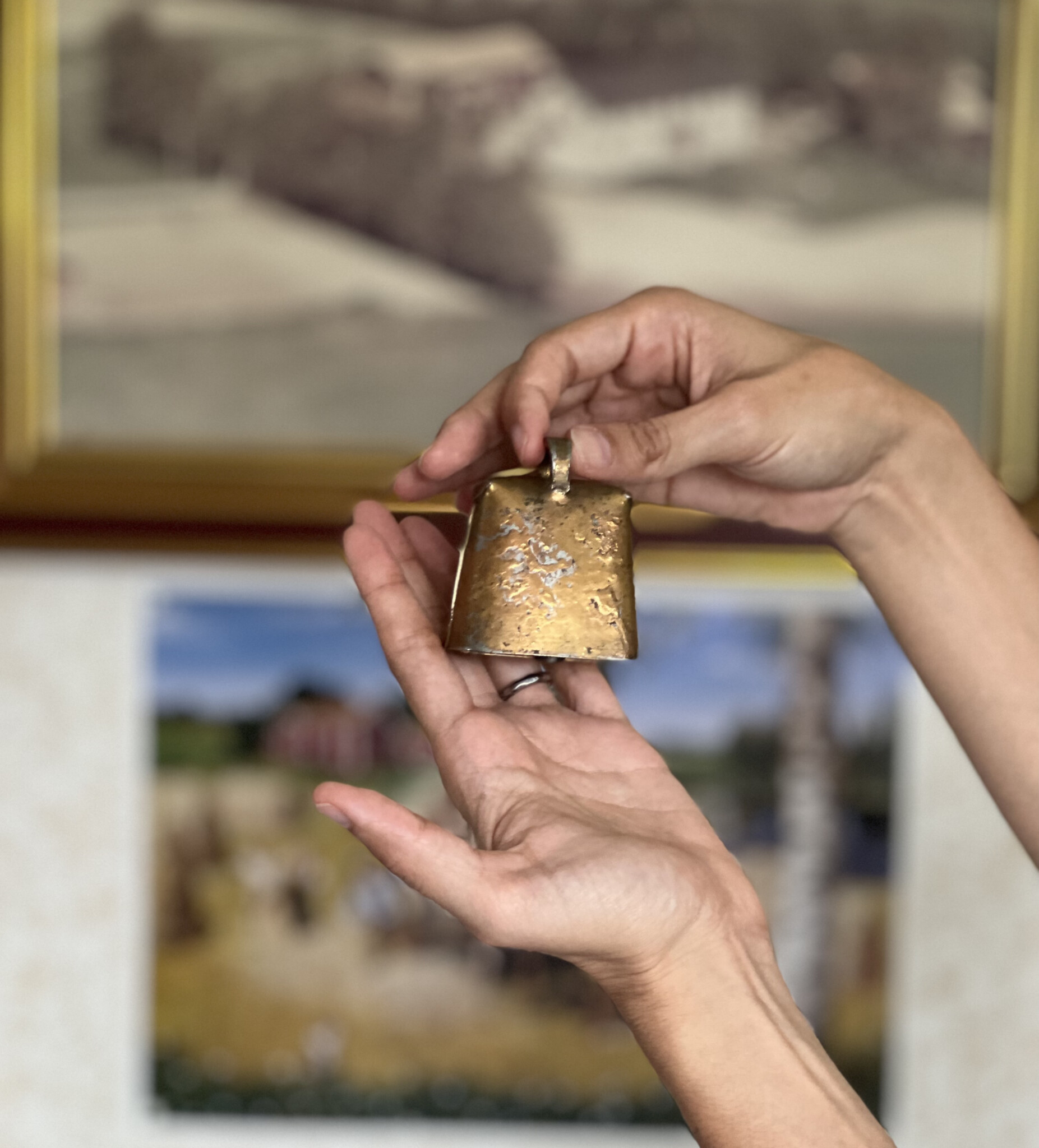 Close up of hands holding a gold sheep bell.