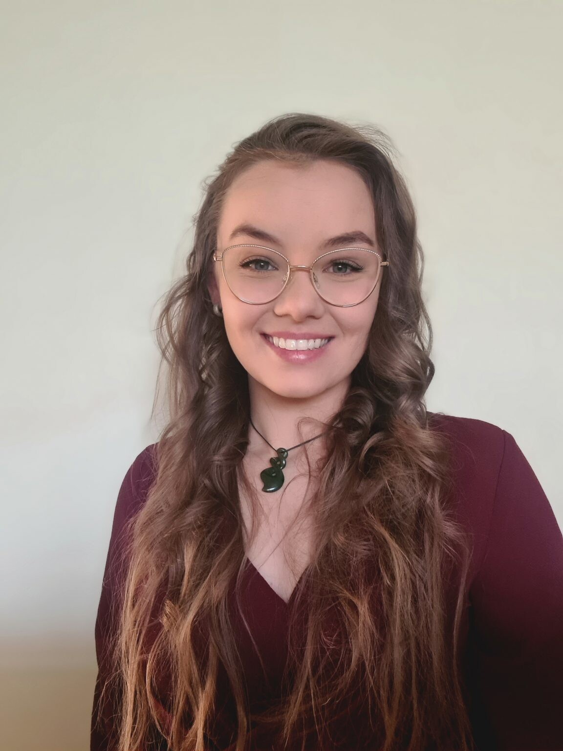 Person with long wavy hair, maroon top, and green pendant necklace