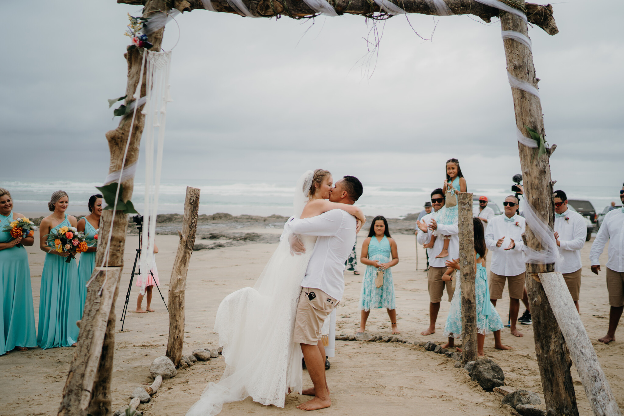 Madeline and her partner kissing under the altar as bridesmaids and groomsmen watch on.