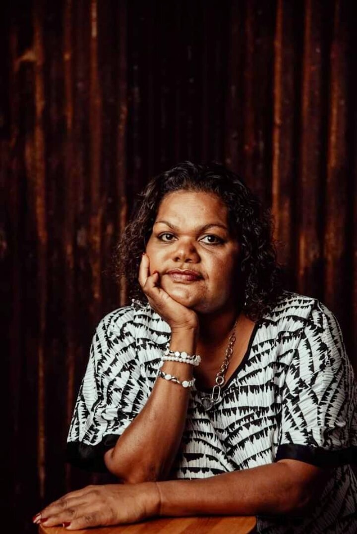 Letisha Shaw, a woman with short curly black hair, she wears a black and white patterned top and rests her hand on her face.