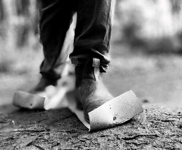 Close-up of Francesco's boots with etching plates attached to the bottom. He is walking in the bush and the ground appears muddy.