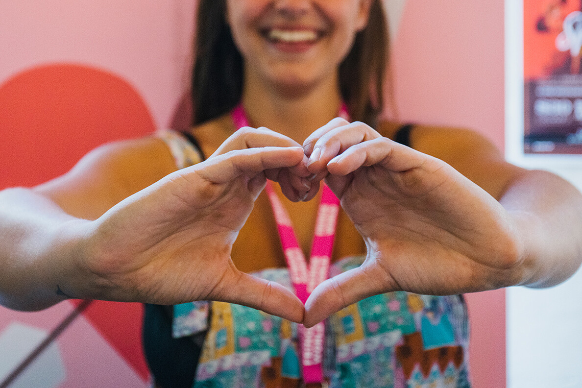 hands held in the shape of a heart, a womans face is obscured but smiling.