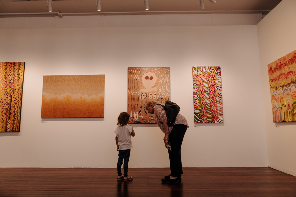 a man and a child stand in a gallery looking at diverse artworks.