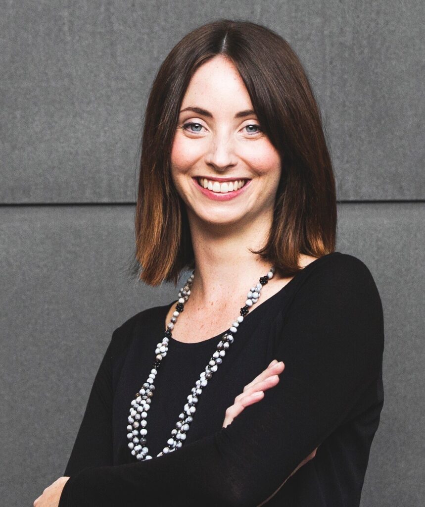 Alysha Saunders, with short brown hair, wearing a black long sleeve top and beaded necklace.