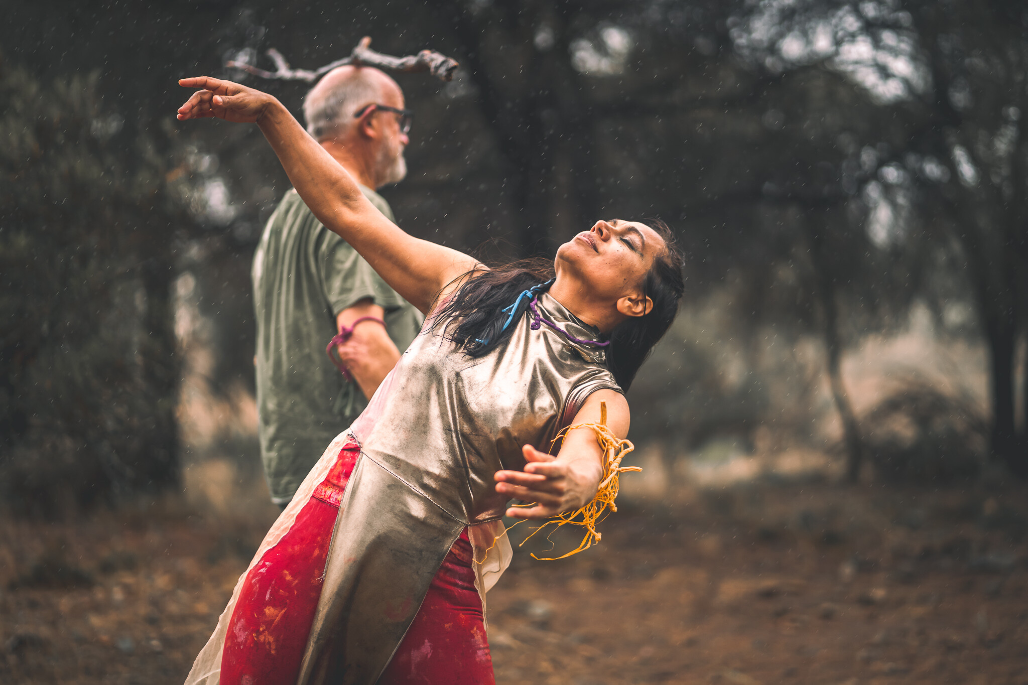 Woman dancing in forground while man balances stick on head in background.
