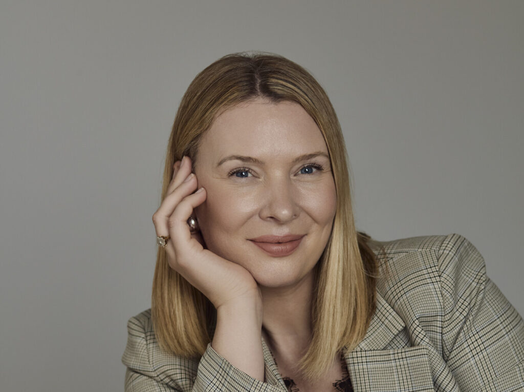 Head shot of a woman with short blonde hair wearing a jacket, smiling at the camera