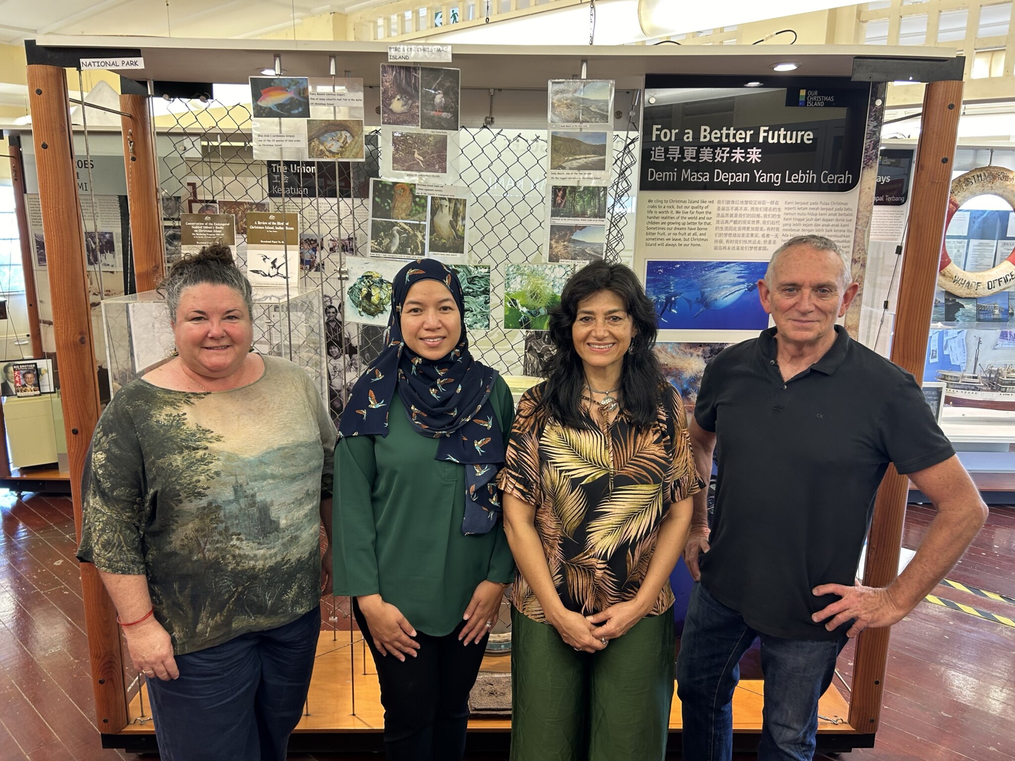 Four people stand before a display board titled "For a Better Future," featuring multilingual text and environmental images.