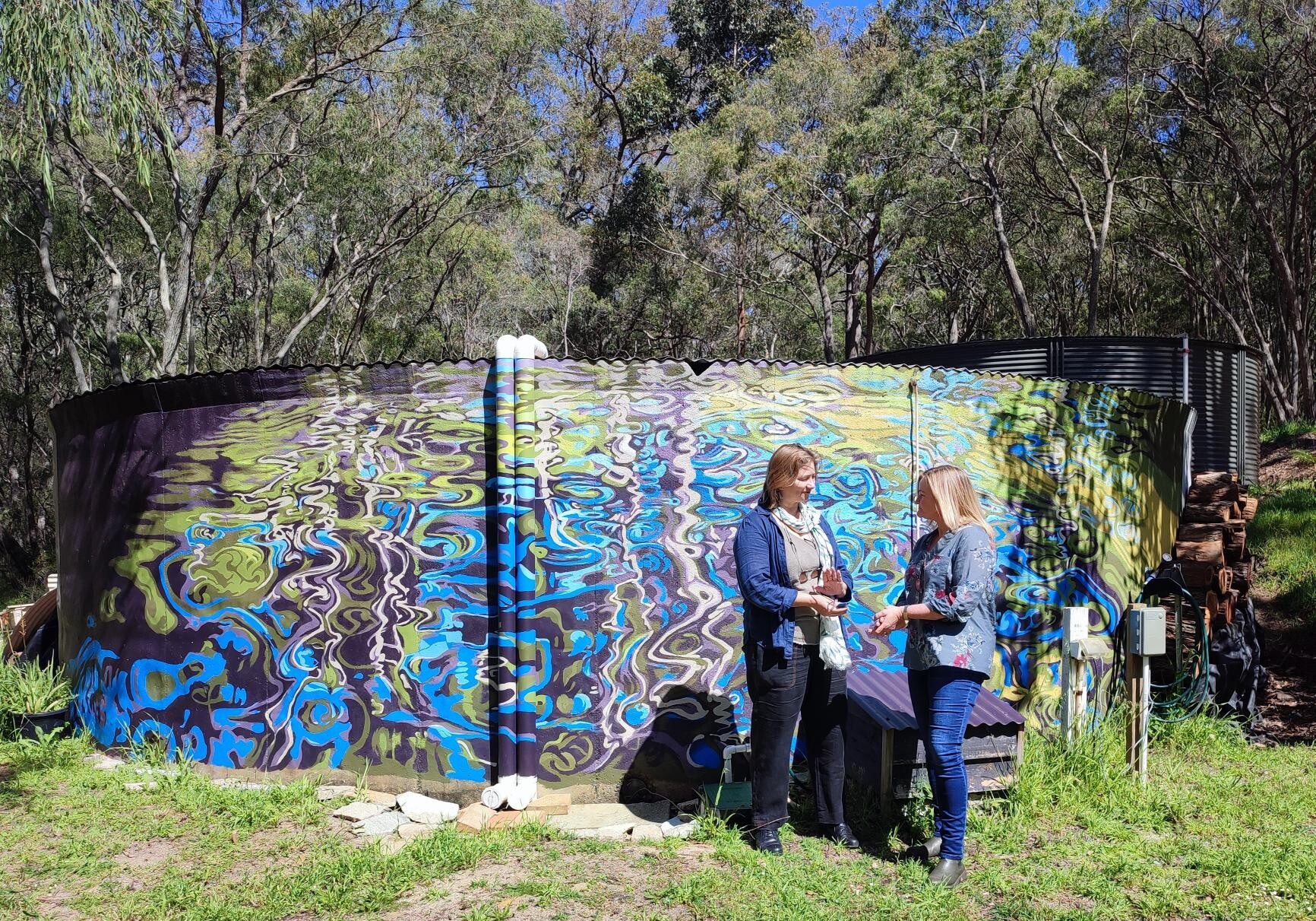 Two women stand in front of a painted water tank to look like water reflections.