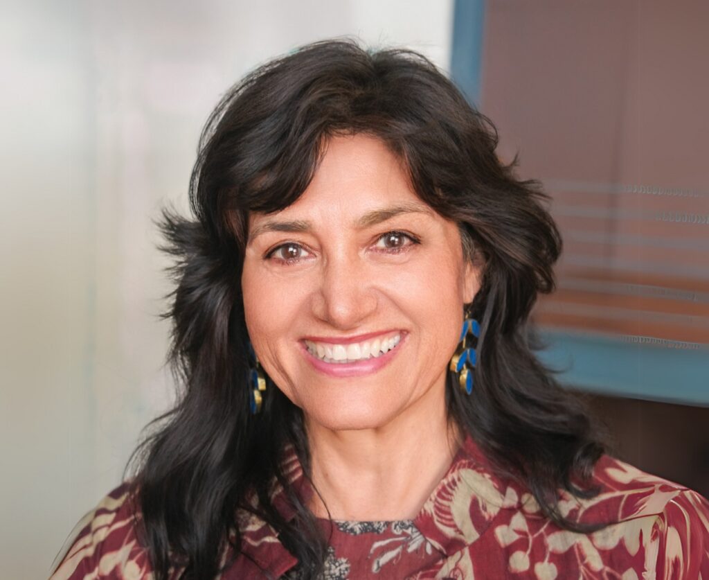 Person with long dark hair, patterned top, and blue earrings
