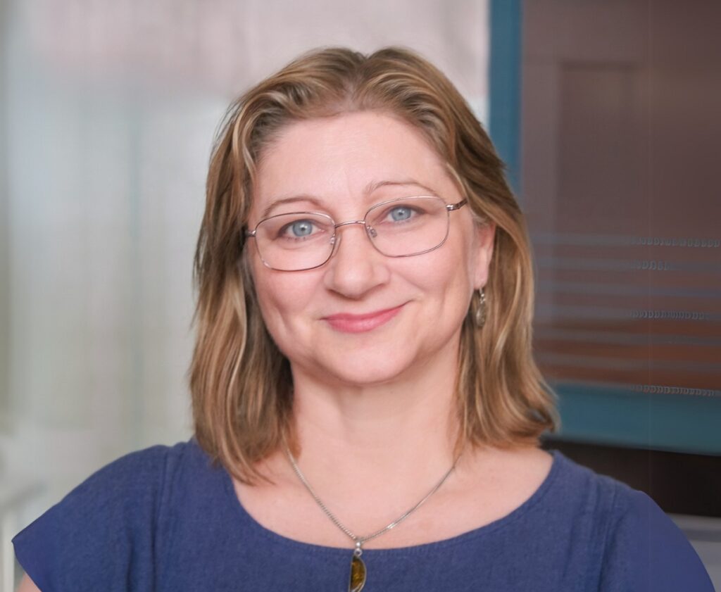 Person with short blonde hair, wearing glasses and a blue top