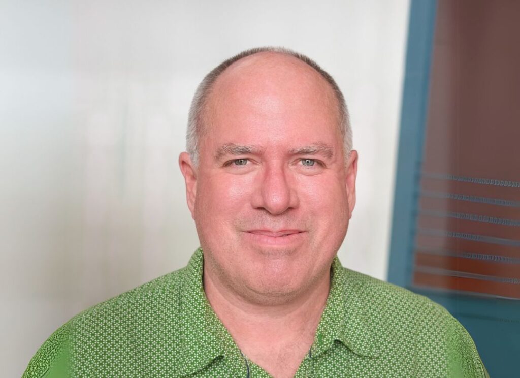 Person with short grey hair wearing a green button up shirt
